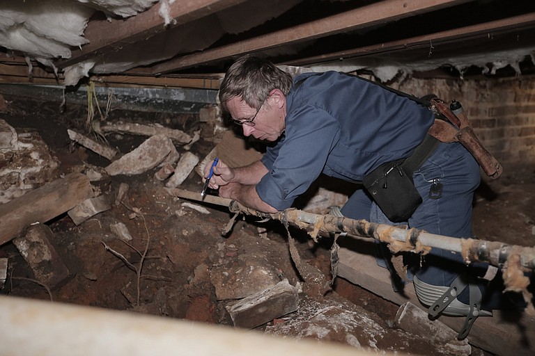 Rick Eades climbs under the foundation of city reporter Tim Summers Jr.’s rental home to check the conditions of the pipes.