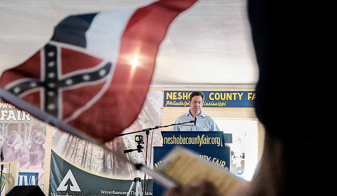 As Republican U.S. Senate candidate Chris McDaniel speaks at the Neshoba County Fair in Philadelphia, Miss., on Aug. 2, 2018, a supporter holds up a replica of the Confederate emblem-bearing Mississippi flag, which McDaniel opposes changing.