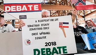 As incumbent Republican U.S. Sen. Cindy Hyde-Smith speaks at the Neshoba County Fair in Philadelphia Miss., on Aug. 2, 2018, supporters of her Republican challenger, Mississippi State Sen. Chris McDaniel, hold up signs calling on her to join him for a debate.