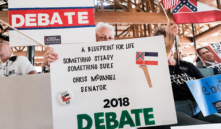 As incumbent Republican U.S. Sen. Cindy Hyde-Smith speaks at the Neshoba County Fair in Philadelphia Miss., on Aug. 2, 2018, supporters of her Republican challenger, Mississippi State Sen. Chris McDaniel, hold up signs calling on her to join him for a debate.