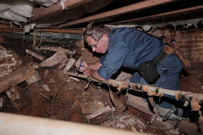 Rick Eades climbs under the foundation of city reporter Tim Summers Jr.'s rental home to check the conditions of the pipes. Photo by Imani Khayyam.