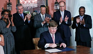 Gov. Tate Reeves signs the bill to remove the state flag. House Speaker Philip Gunn and Lt. Gov. Delbert Hosemann, both now infected with COVID-19, stand behind him. Dr. Thomas Dobbs now says Mississippi needs mask mandates. Photo by Rogelio V. Solis via AP