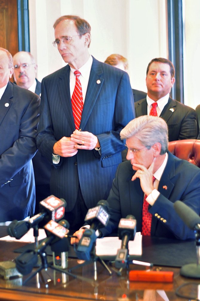 Gov. Phil Bryant (sitting) signed the legislation to implement voter ID in Mississippi.
