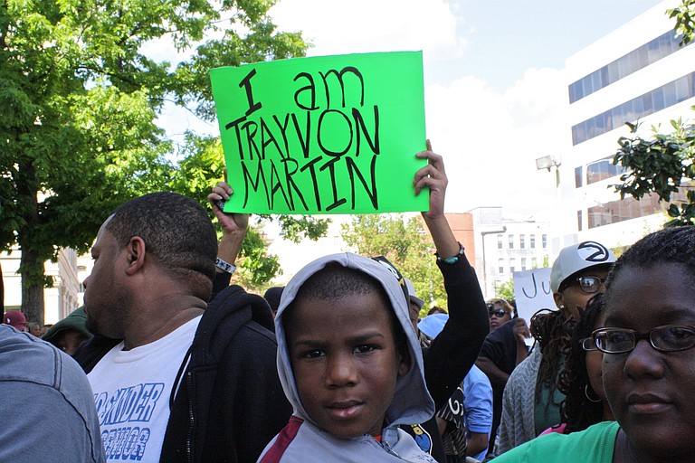 A woman holds a young protester, dressed in a gray hoodie, in front of City Hall Sunday.