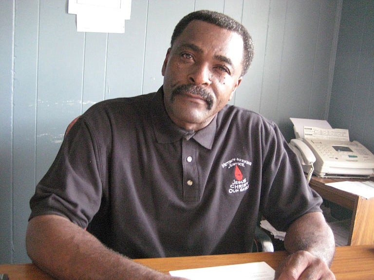 Larry Nelson Sr., at his desk at Hometown Auto Sales on Robinson Road, is offering a $10,000 reward to find who killed his son, Larry Nelson Jr.